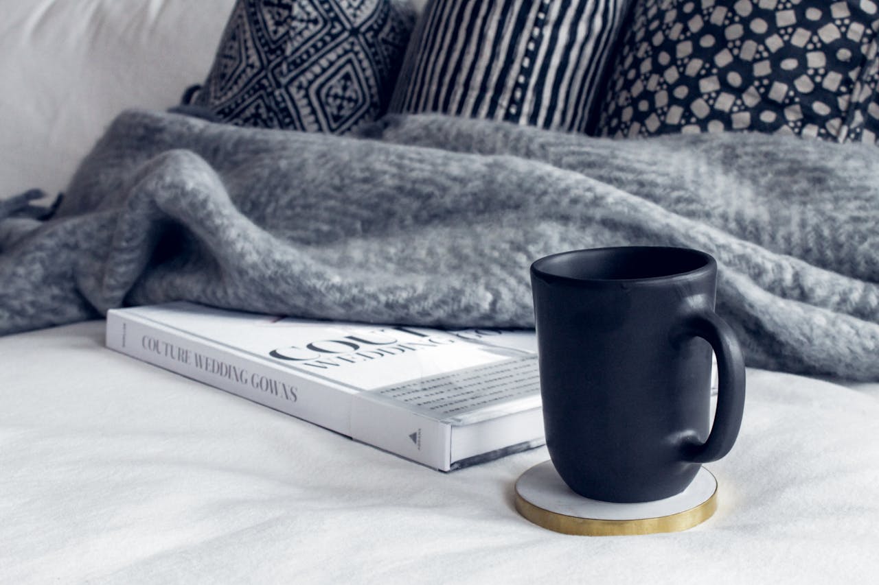 A cozy interior scene featuring a black mug, a book, and patterned pillows on a soft couch.